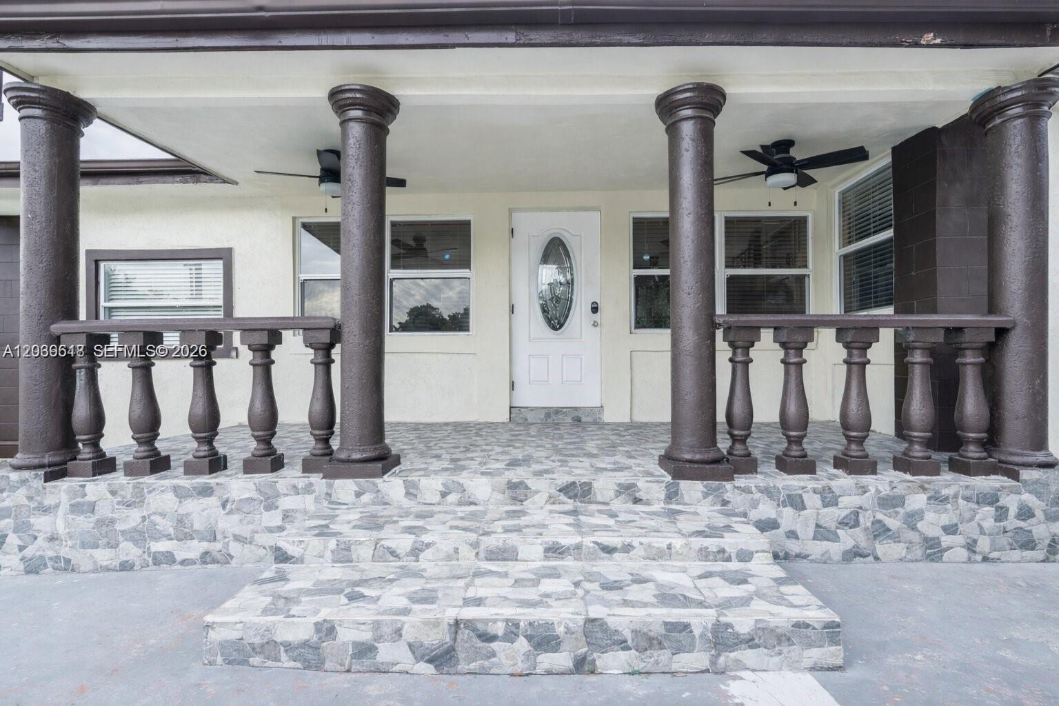 A covered front porch features stone-tiled steps, dark brown columns, and a white front door — 65 NW 118th St, Miami FL 33168, MIAMI, FL