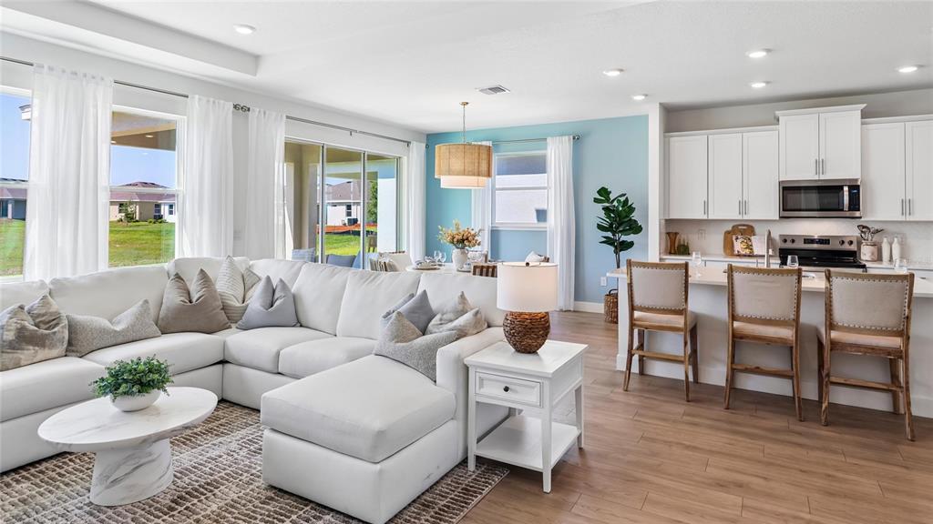 A bright open-concept living room and kitchen feature white cabinetry, light wood floors, and furniture — 1627 NW 128TH TERRACE, NEWBERRY, FL