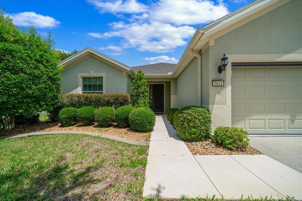 A single-story house exterior features a beige stucco facade, a garage, and manicured landscaping — 9841 SW 75TH STREET ROAD, OCALA, FL