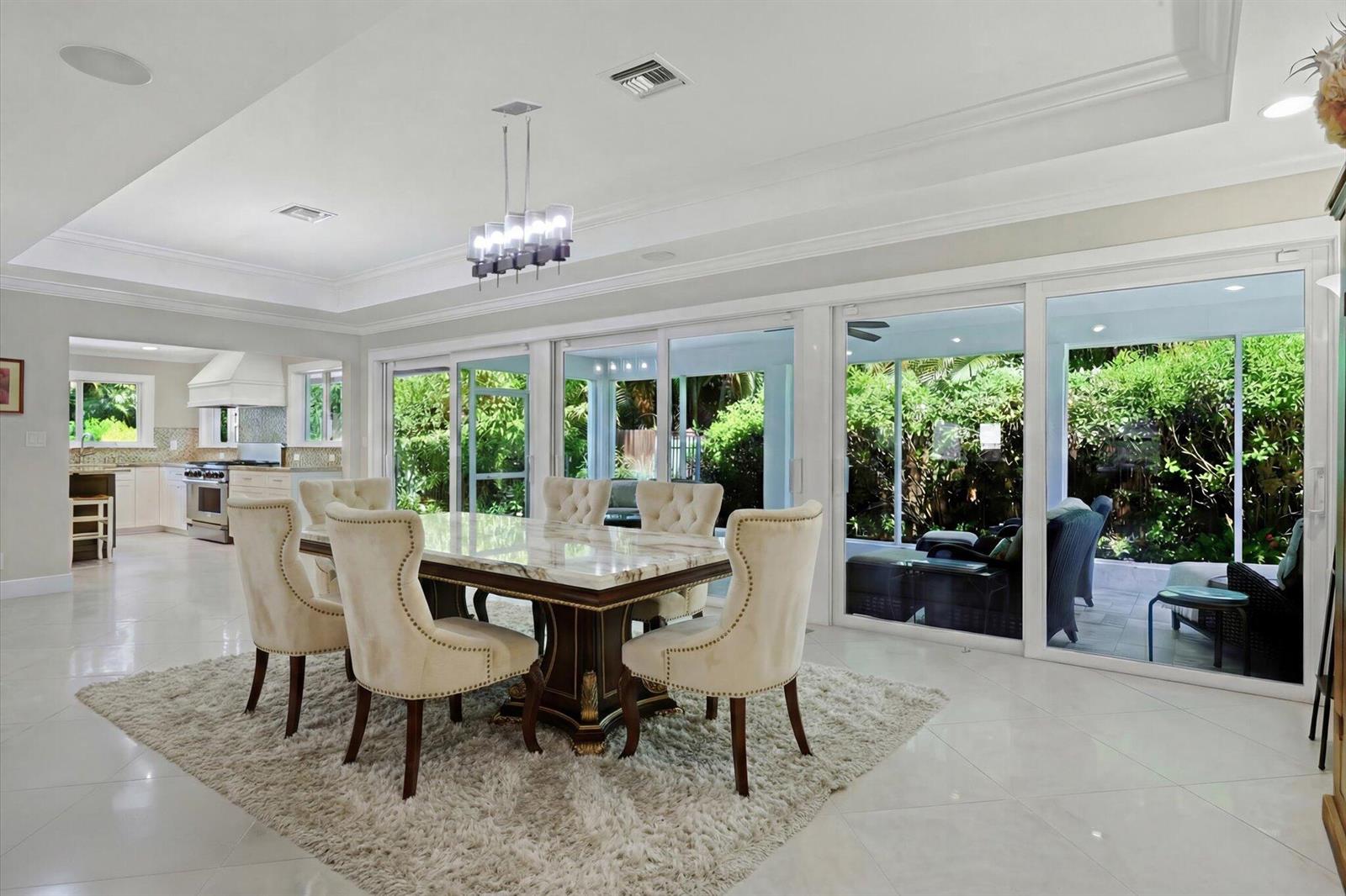 A dining room with a marble-topped table, tufted chairs, and sliding doors opening to a patio — 4535 Oak Tree Court, Delray Beach FL 33445, DELRAY BEACH, FL