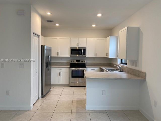 A kitchen features white cabinets, stainless steel appliances, and a peninsula counter with tile flooring — 20626 NE 5th Pl # 20626, Miami FL 33179, MIAMI, FL