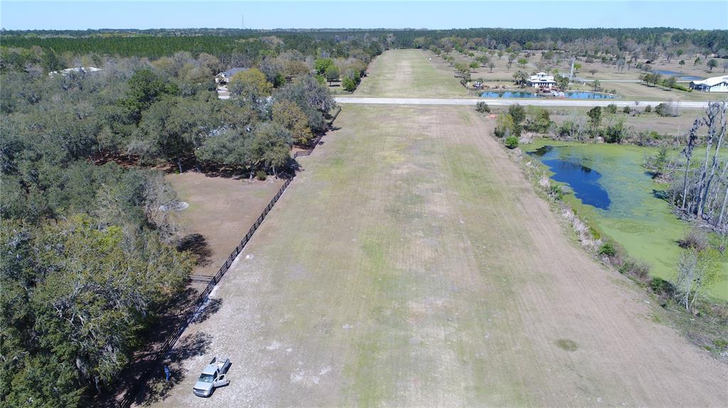 An aerial view shows a long, grassy runway bordered by trees, a fence, and ponds — Parcel 2 SW 128TH ROAD, WORTHINGTON SPRINGS, FL