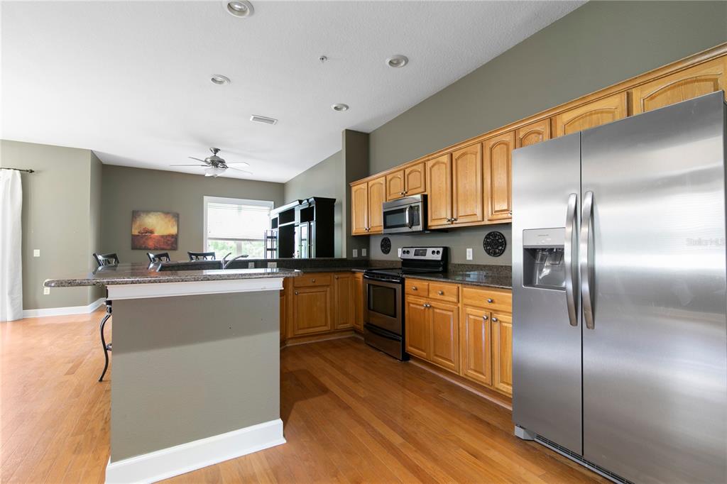 A kitchen features wood cabinets, stainless steel appliances, granite countertops, and hardwood flooring — 11504 BELLAMAR STREET, TAMPA, FL