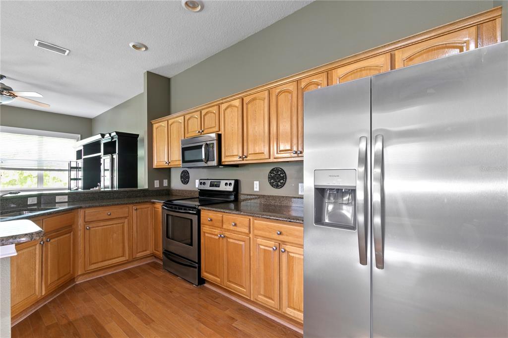 A kitchen features light wood cabinets, stainless steel appliances, and dark granite countertops — 11504 BELLAMAR STREET, TAMPA, FL