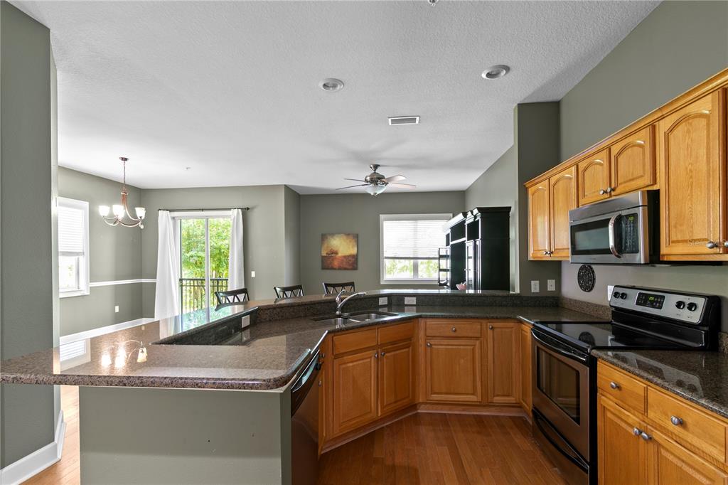 A kitchen with wood cabinets, granite countertops, and stainless steel appliances overlooks an adjacent dining area — 11504 BELLAMAR STREET, TAMPA, FL