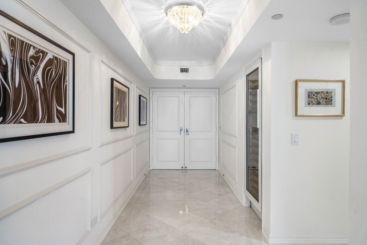 A bright hallway features white paneled walls, a crystal chandelier, and a tiled floor — 3211 S Ocean Boulevard # 903, Highland Beach FL 33487, HIGHLAND BEACH, FL