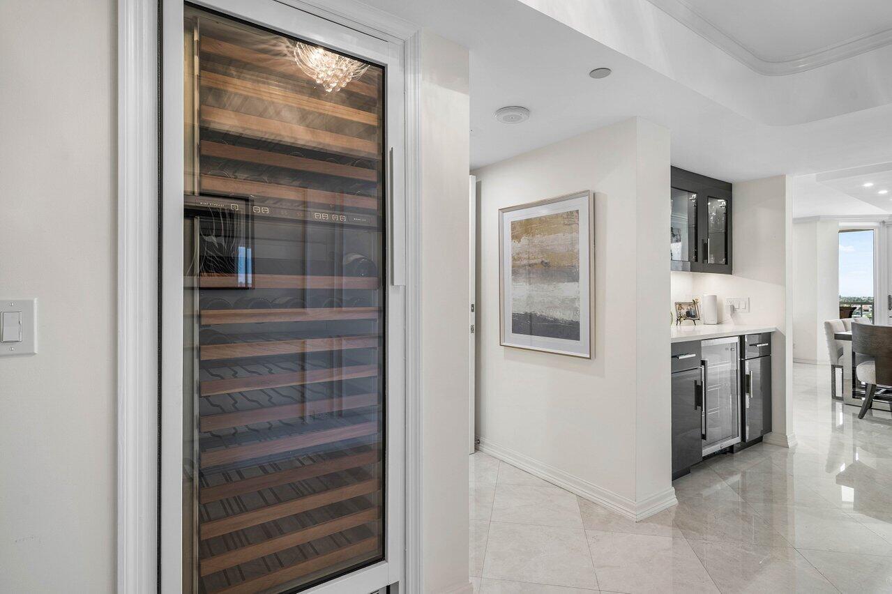 A tall wine refrigerator stands in a hallway next to a kitchen with dark cabinetry — 3211 S Ocean Boulevard # 903, Highland Beach FL 33487, HIGHLAND BEACH, FL
