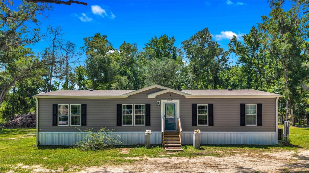 A single-story manufactured home with grey siding and black shutters sits on a grassy lot — 24050 CORTEZ BOULEVARD, BROOKSVILLE, FL