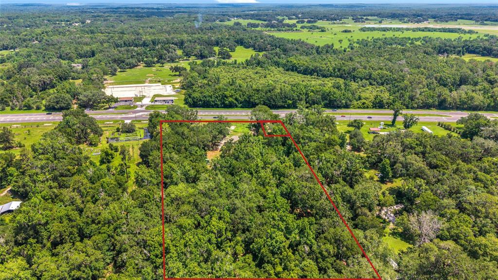 An aerial view shows a wooded plot of land outlined in red near a highway — 24050 CORTEZ BOULEVARD, BROOKSVILLE, FL