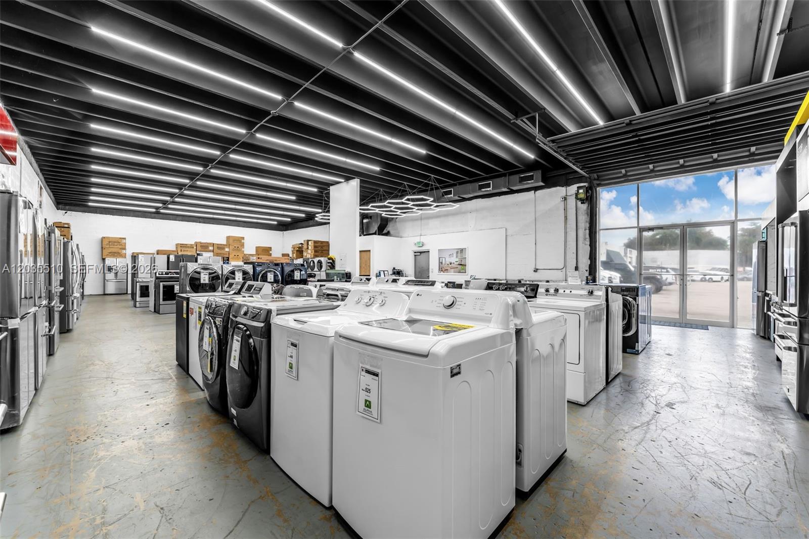 A warehouse showroom displays rows of various household appliances under industrial ceiling lighting — 12134 SW 114 Place, Miami FL 33176, MIAMI, FL