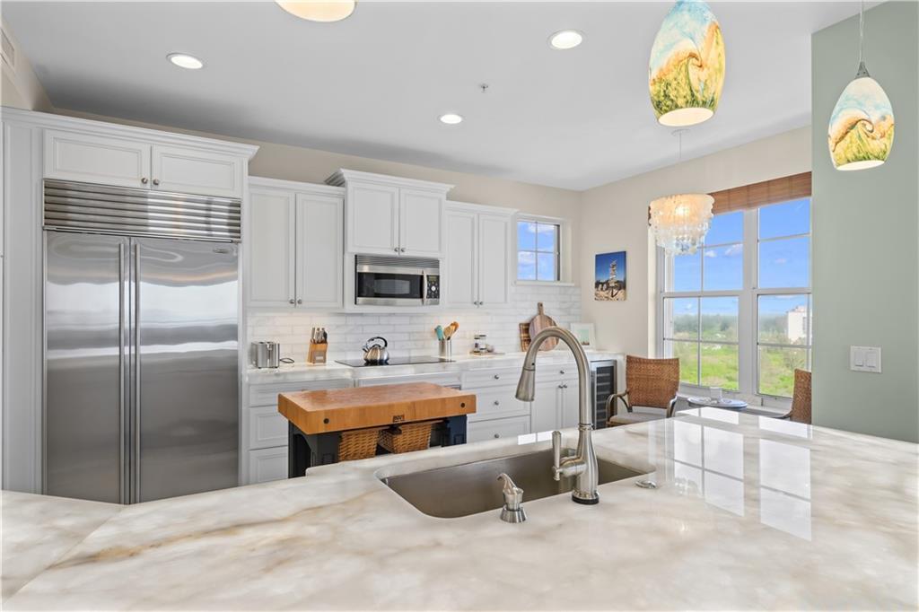 A kitchen features white cabinetry, stainless steel appliances, a marble island, and a window view — HUTCHINSON ISLAND, FL
