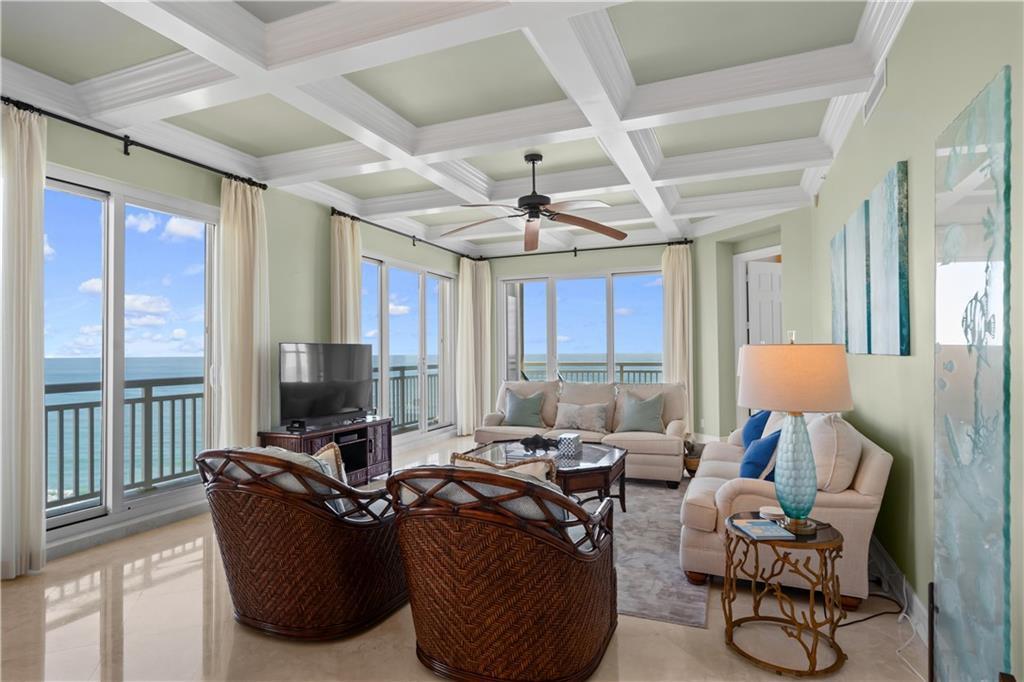 A living room with a coffered ceiling, wicker chairs, and floor-to-ceiling windows overlooking the ocean — HUTCHINSON ISLAND, FL