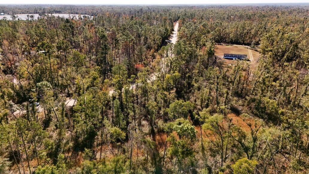 An aerial view shows a rural property with a house, a dirt road, and dense forest — Lot 7 NW 27th Terrace, FL 32053, FL