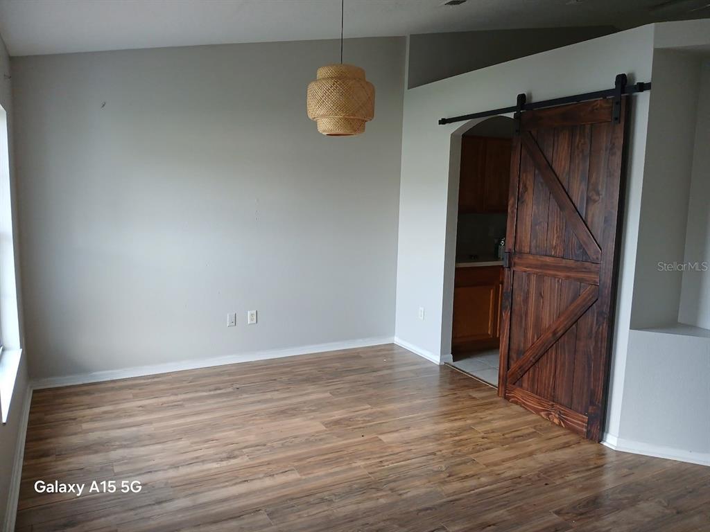A room with wood-look flooring, a woven pendant light, and a dark wood barn door — 7500 LULLWATER AVENUE, SPRING HILL, FL