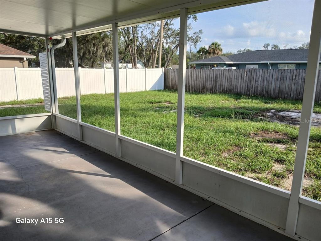 A screened-in concrete patio overlooks a grassy backyard enclosed by a white vinyl fence — 7500 LULLWATER AVENUE, SPRING HILL, FL