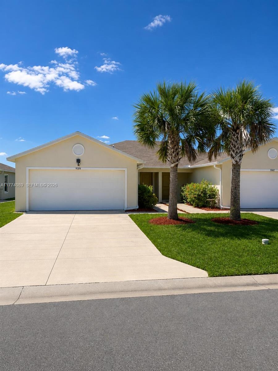 A single-story house with a two-car garage, two palm trees, and a concrete driveway — 9084 Aegean Cir, Lehigh Acres FL 33936, LEHIGH ACRES, FL