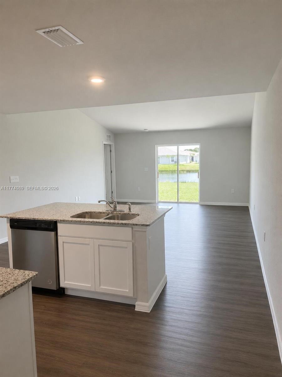 A kitchen island with a stainless steel dishwasher faces an open living area with sliding doors — 9084 Aegean Cir, Lehigh Acres FL 33936, LEHIGH ACRES, FL