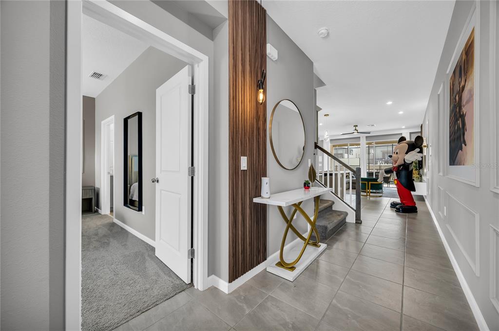 A hallway with tile flooring leads to a staircase, a console table, and a Mickey statue — 2362 ZABALLINA PLACE, KISSIMMEE, FL