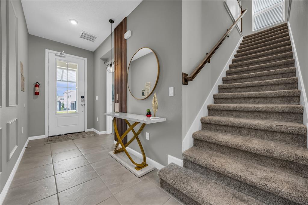 An entryway features tiled floors, a console table, a round mirror, and carpeted stairs — 2362 ZABALLINA PLACE, KISSIMMEE, FL