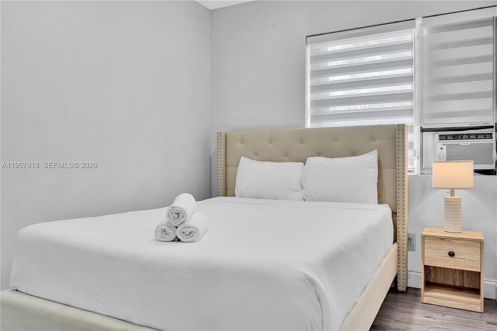 A bedroom features a tufted beige headboard, white bedding with rolled towels, and a window unit — 10002 E Bay Harbor Dr # 6, Bay Harbor Islands FL 33154, BAY HARBOR ISLANDS, FL
