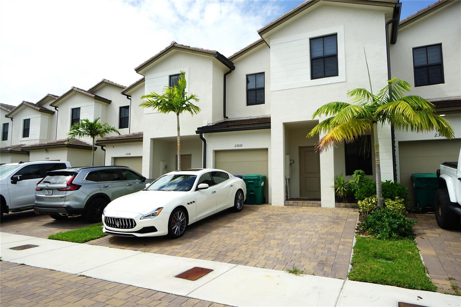 A row of multi-story townhomes with paved driveways and parked cars under a cloudy sky — 23010 SW 128th Place # 23010, Miami FL 33170, MIAMI, FL