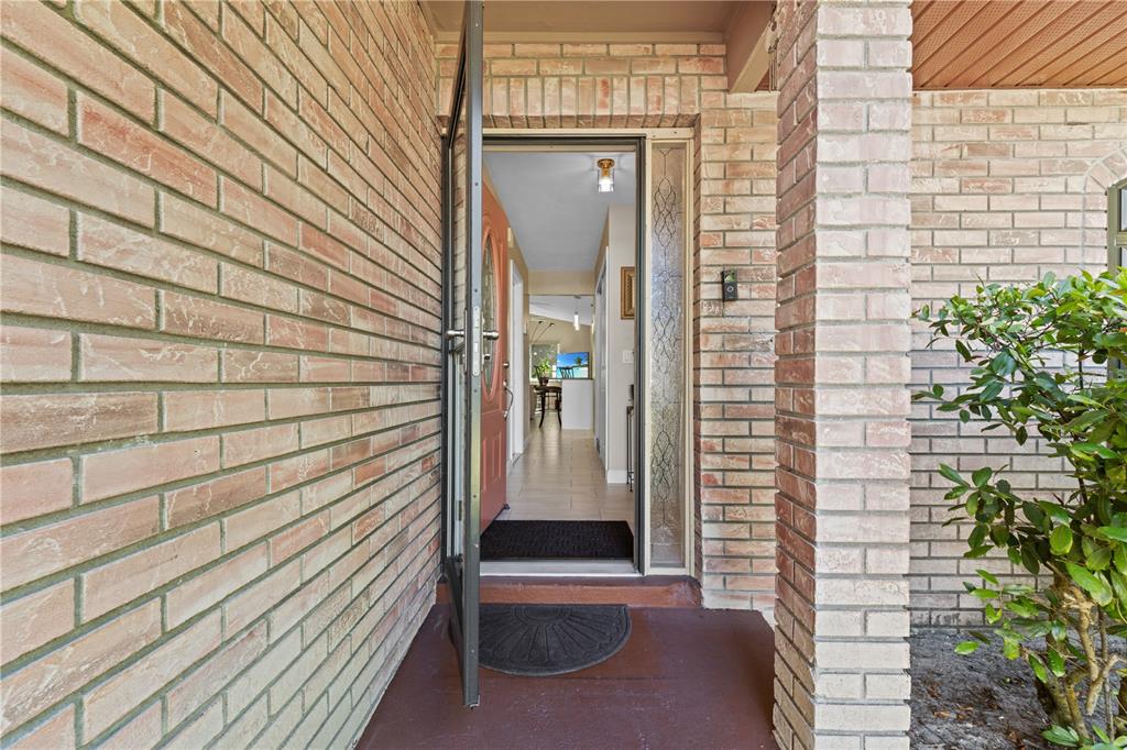 A brick-walled entryway features a storm door opening into a tiled interior hallway — 283 CHESTNUT AVENUE, ORANGE CITY, FL
