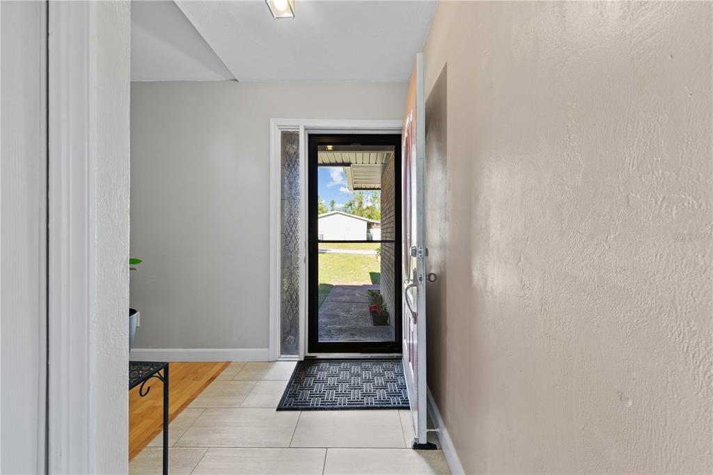 An entryway with light-colored tile flooring, a glass storm door, and a beige wall — 283 CHESTNUT AVENUE, ORANGE CITY, FL
