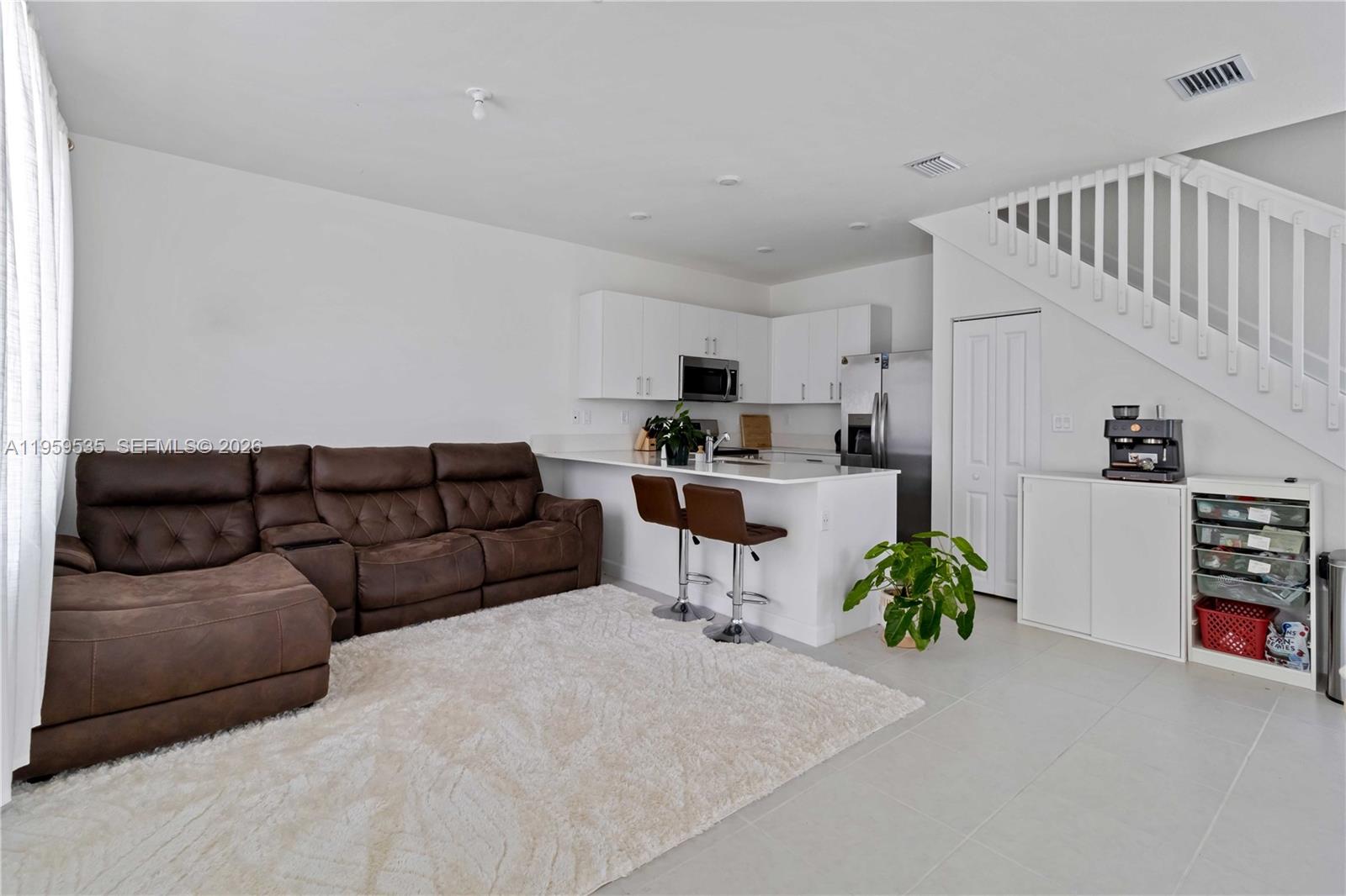 A living room with a brown sectional, white kitchen cabinetry, and a staircase — 760 SE 13th Ct, Homestead FL 33034, HOMESTEAD, FL