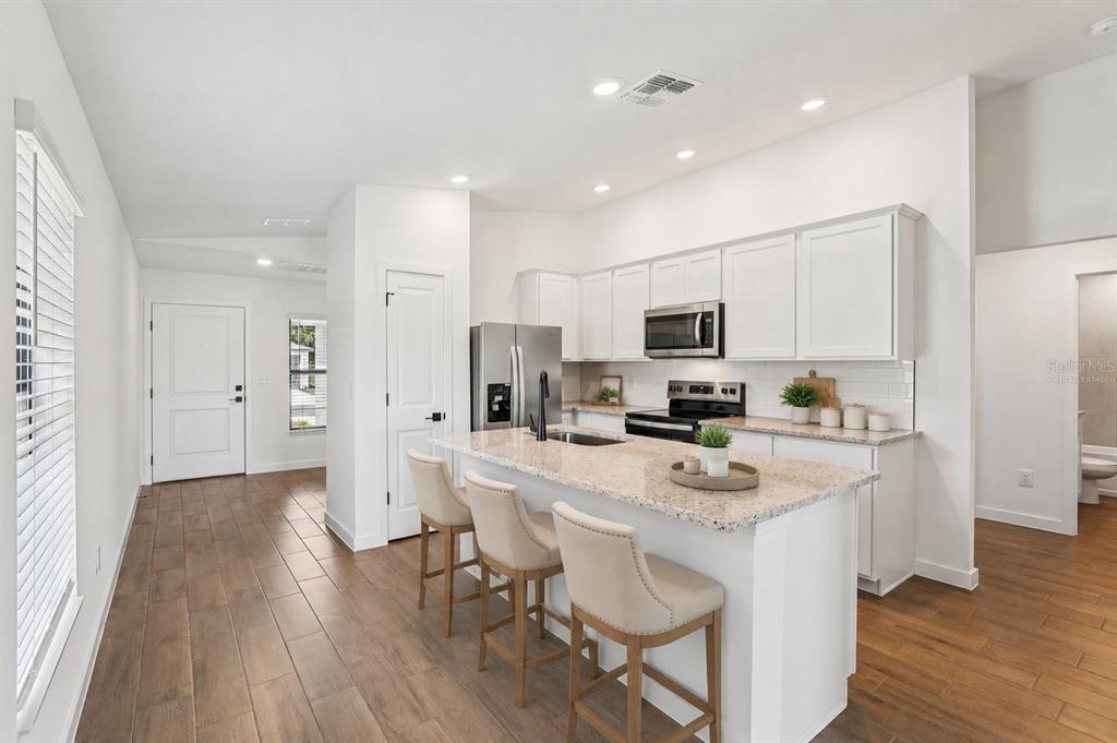 A kitchen features white cabinets, granite countertops, a center island with stools, and wood flooring — 12249 SHAFTON ROAD, SPRING HILL, FL