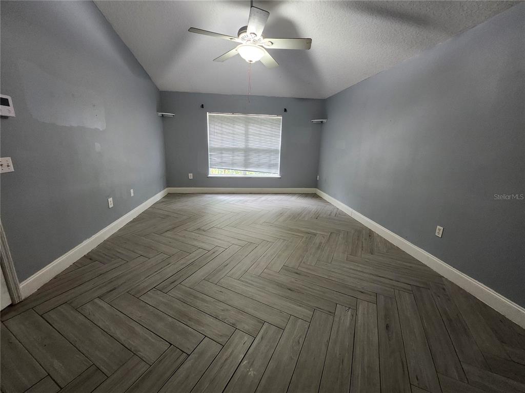 An empty room features gray walls, a vaulted ceiling with a fan, and herringbone flooring — 2200 EL MARRA DRIVE, OCOEE, FL
