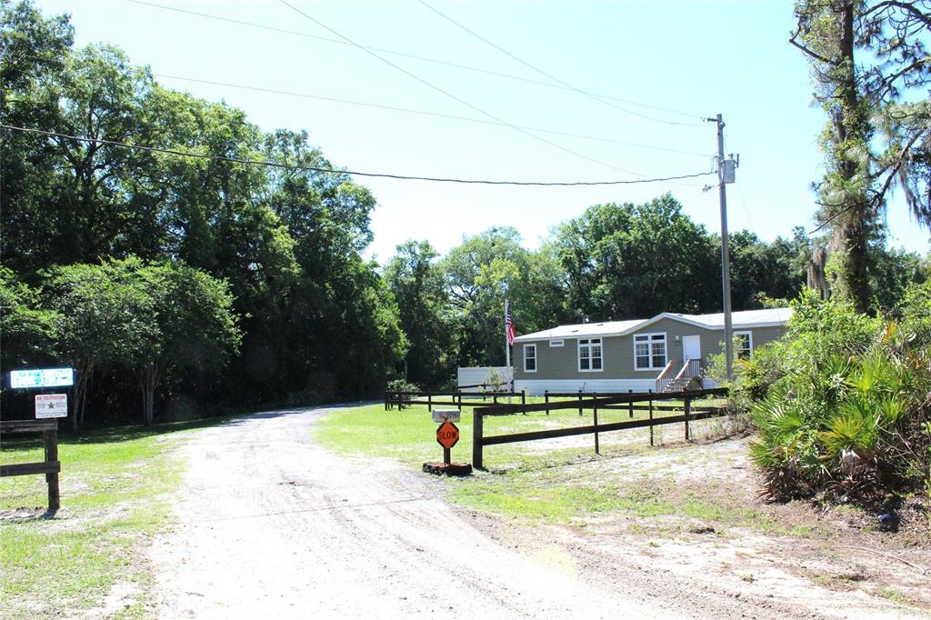 A mobile home sits behind a wooden fence along a dirt driveway surrounded by trees — 175 E SAN JOSE STREET, PALATKA, FL