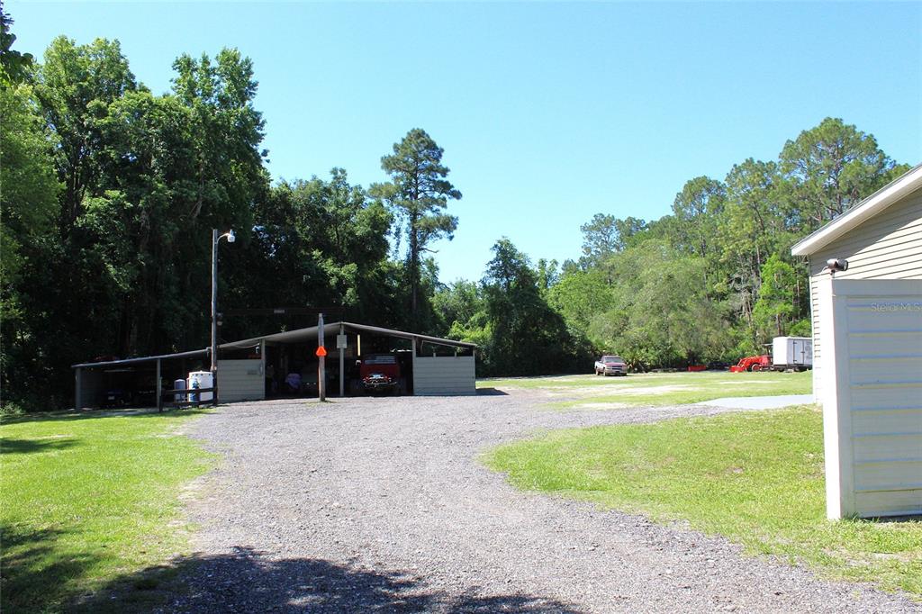 A gravel driveway leads to a large metal carport structure on a wooded lot — 175 E SAN JOSE STREET, PALATKA, FL