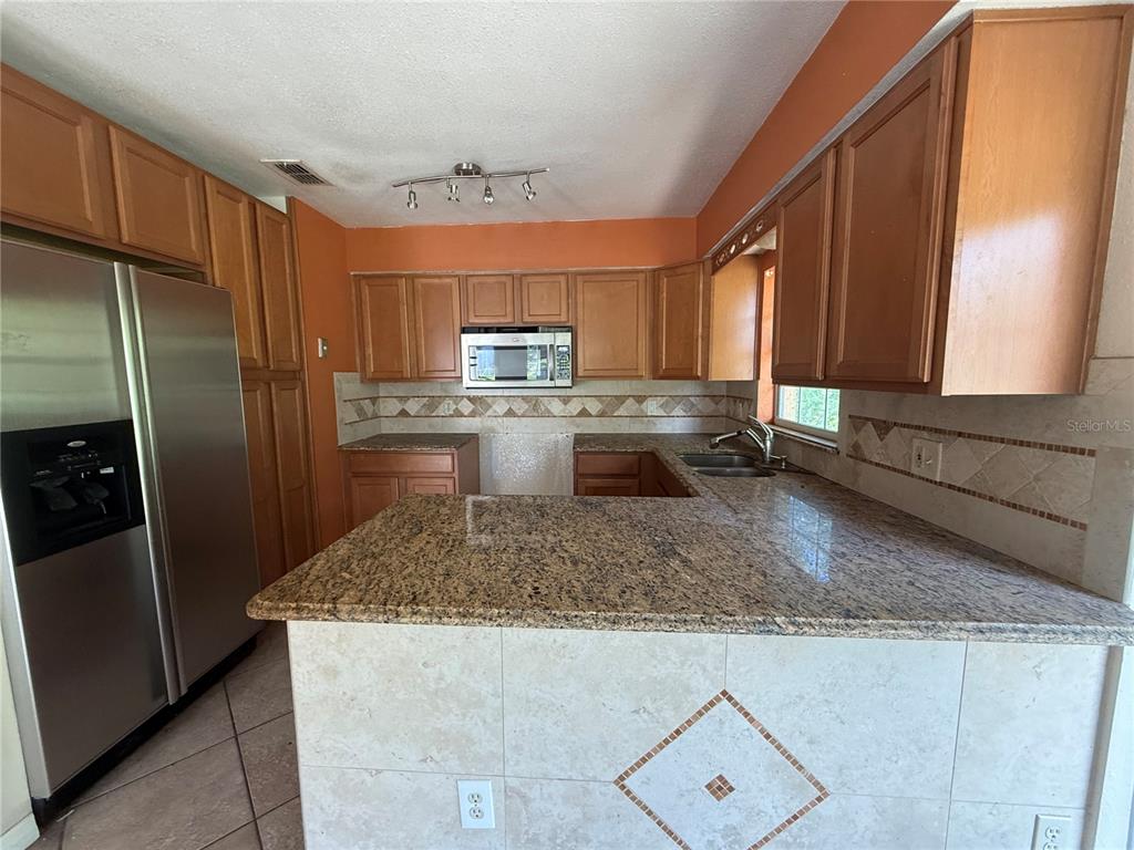 A kitchen features wood cabinets, granite countertops, a stainless steel refrigerator, and orange walls — 5710 JOYCE STREET, ORLANDO, FL