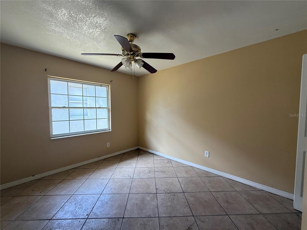 An empty bedroom features tan walls, a ceiling fan, and light-colored tile flooring — 5710 JOYCE STREET, ORLANDO, FL