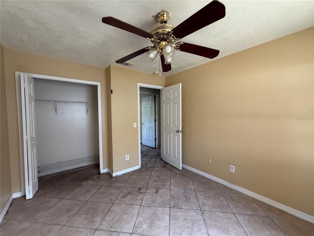 An empty bedroom features tan walls, a ceiling fan, and light-colored diagonal floor tiles — 5710 JOYCE STREET, ORLANDO, FL