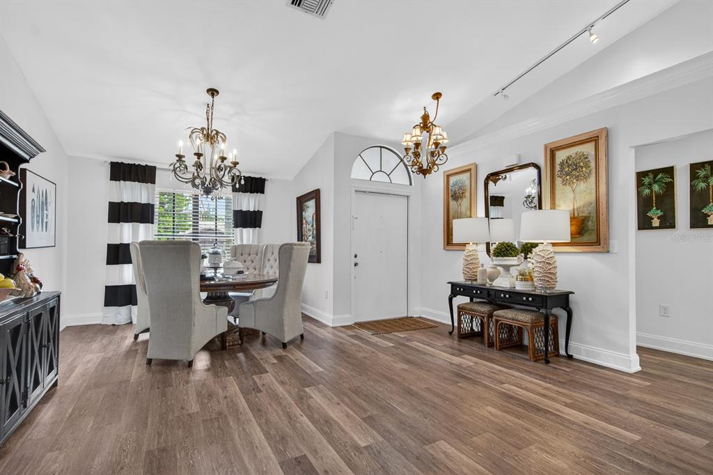A dining area and entryway feature wood-look flooring, two chandeliers, and a black console table — 16 CITRUS DRIVE, PALM HARBOR, FL
