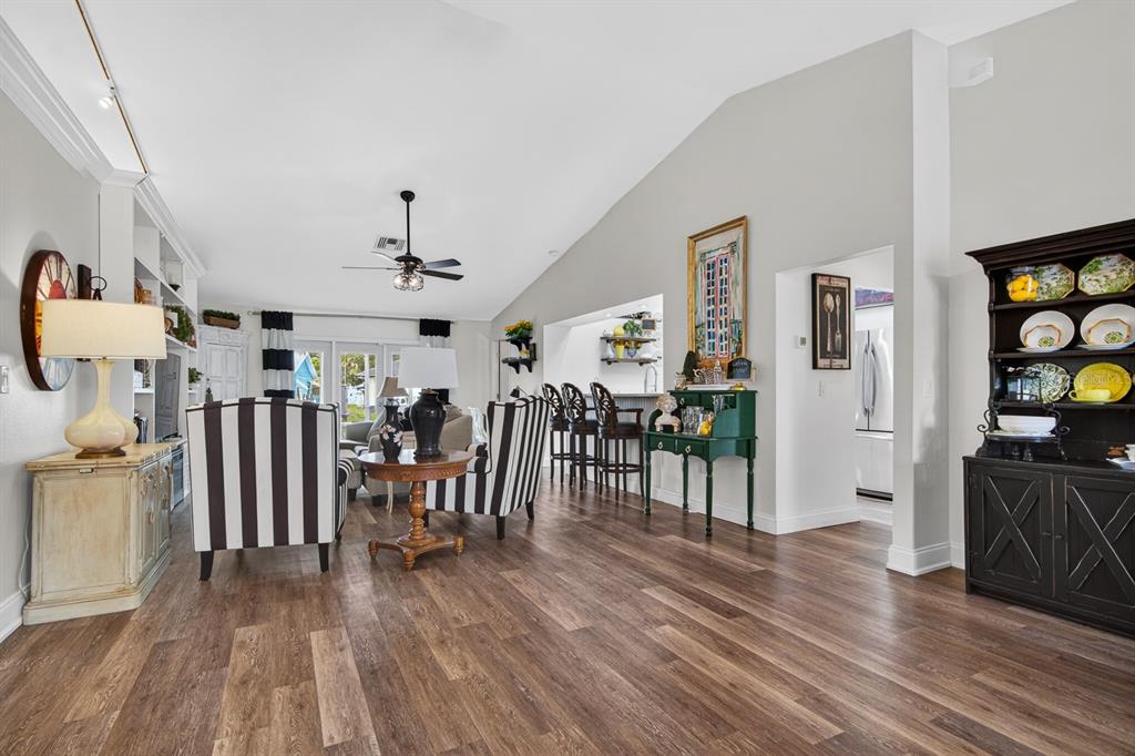 A living room with wood-look flooring, vaulted ceilings, striped armchairs, and a dark hutch — 16 CITRUS DRIVE, PALM HARBOR, FL