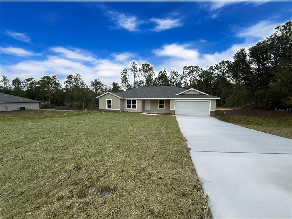A single-story house with a two-car garage and a concrete driveway sits on a lawn — 12297 SW 87TH STREET, DUNNELLON, FL