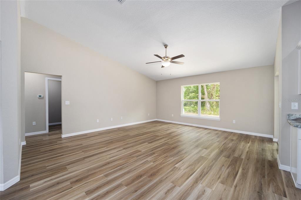 A spacious living room features light-colored walls, wood-look flooring, a vaulted ceiling, and a ceiling fan — 12297 SW 87TH STREET, DUNNELLON, FL