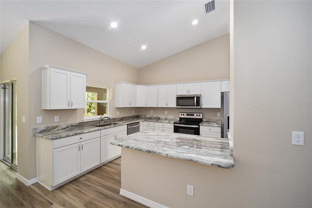 A kitchen with white cabinets, marble-patterned countertops, stainless steel appliances, and wood-look flooring — 12297 SW 87TH STREET, DUNNELLON, FL