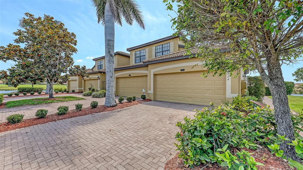 A multi-unit residential building features tan stucco walls, tiled roofs, and paved driveways — 7124 GRAND ESTUARY TRAIL UNIT 104, BRADENTON, FL