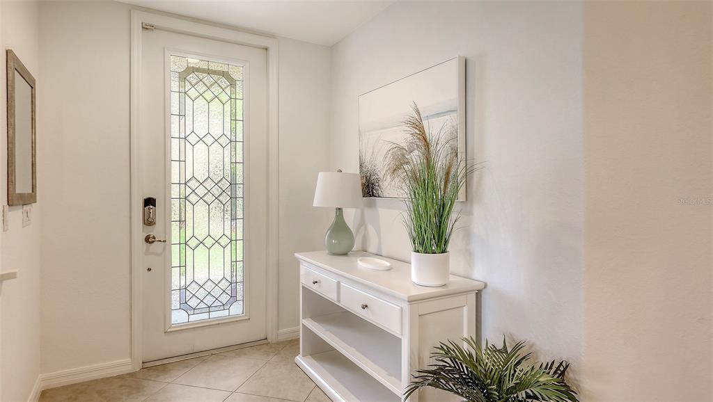 A bright entryway features a white console table, a decorative lamp, and a glass-paneled front door — 7124 GRAND ESTUARY TRAIL UNIT 104, BRADENTON, FL