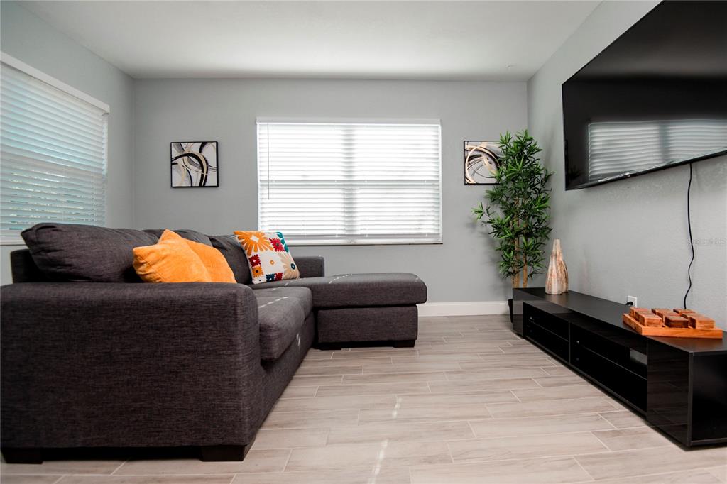 A living room features a gray sectional sofa, a black media console, and light-colored tile flooring — 3147 W CORDELIA STREET, TAMPA, FL