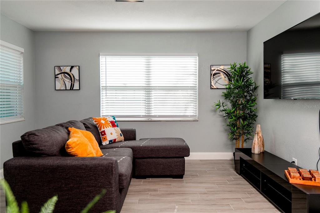 A living room features a dark gray sectional sofa, a television, and light wood-look flooring — 3147 W CORDELIA STREET, TAMPA, FL
