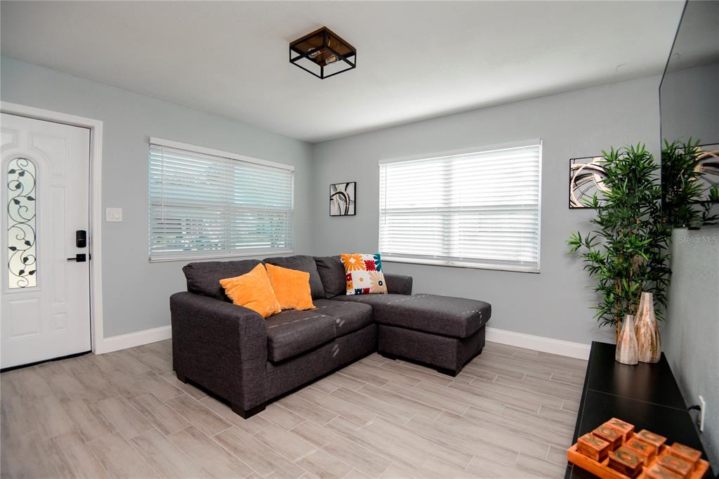 A living room features a gray sectional sofa, light wood-look tile flooring, and two windows — 3147 W CORDELIA STREET, TAMPA, FL