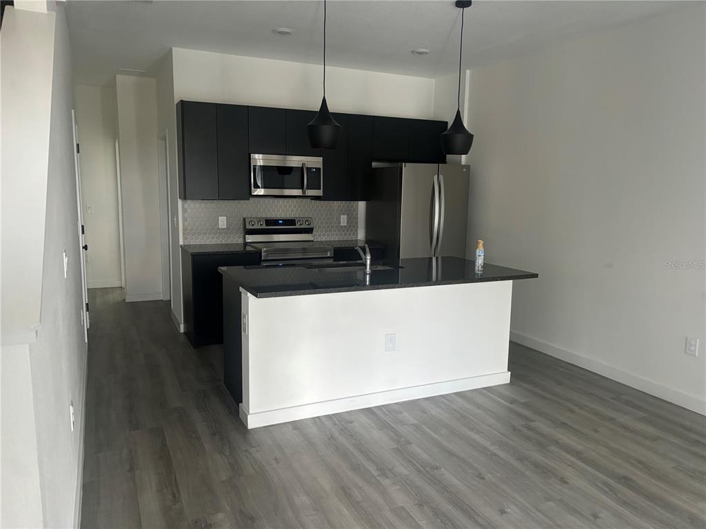 A modern kitchen features dark cabinets, stainless steel appliances, a kitchen island, and gray flooring — 3357 TRANQUIL TRAIL, KISSIMMEE, FL
