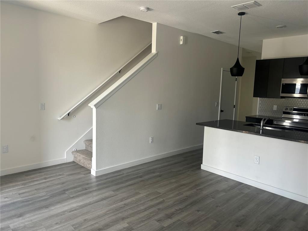 An open-concept kitchen with dark cabinets and a breakfast bar sits beside a carpeted staircase — 3357 TRANQUIL TRAIL, KISSIMMEE, FL