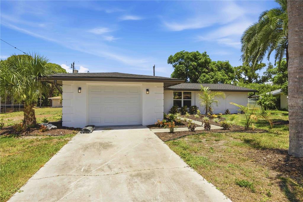A white, single-story house with a one-car garage, a concrete driveway, and palm trees — 386 CABANA ROAD, VENICE, FL