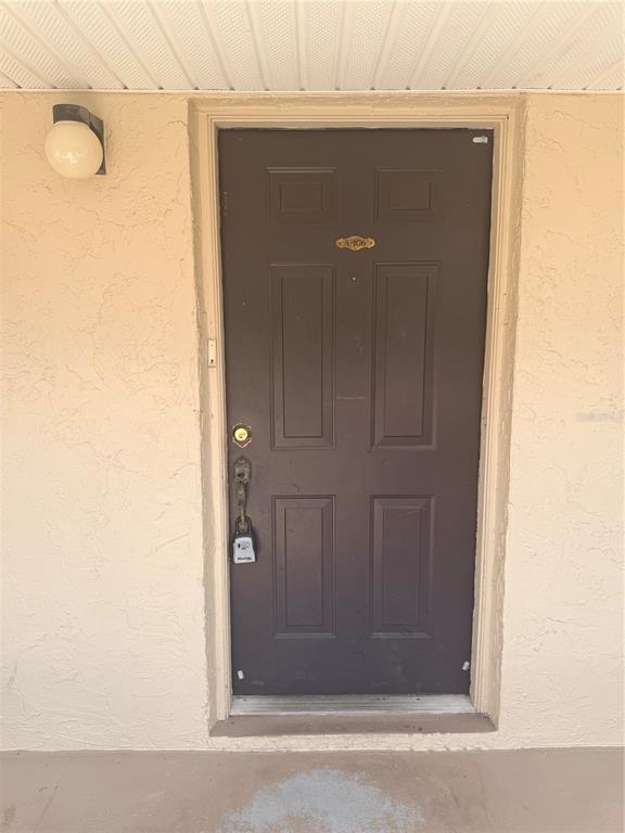 A brown front door with a lockbox is set into a beige stucco exterior wall — 100 E KENTUCKY AVENUE UNIT A106, DELAND, FL