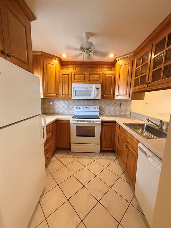 A galley kitchen features light wood cabinets, white appliances, and a tiled floor — 100 E KENTUCKY AVENUE UNIT A106, DELAND, FL